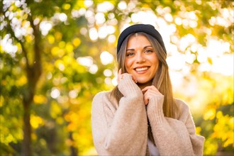 Young blonde girl with a wool cap in autumn at sunset in a natural park smiling