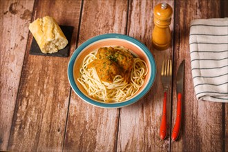 Plate of meatballs with spaghetti with cutlery and bread and pepper shaker on a wooden table