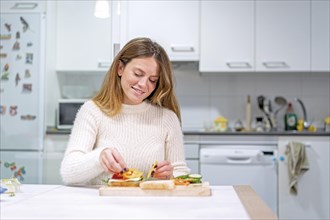 Vegetarian woman cooking a vegetable sandwich in the kitchen at home. Preparing it by putting tomato