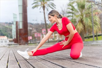 Fit woman in red clothes doing stretching in a city park in spring
