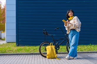 Portrait of Asian girl listening to music with yellow headphones on a blue college background