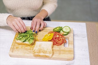 Unrecognizable person cooking a vegetable sandwich in the kitchen at home. Placing the arugula