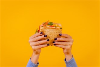 Hands of a woman with a sandwich on a yellow background
