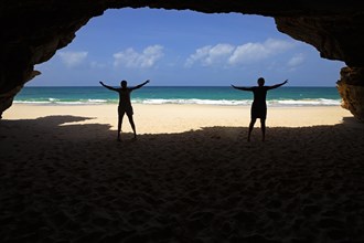 Two tourists silhouetted at entrance of sea cave at Praia de Santa Monica