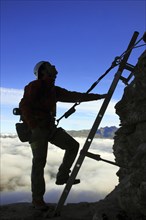 Silhouette of mountain climber climbing metal ladder of Via ferrata in the Swiss Alps