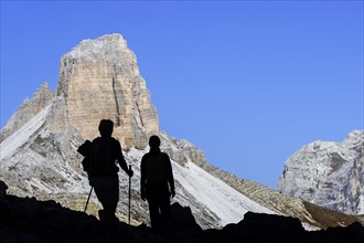 Two mountain walkers silhouetted against Torre dei Scarperi