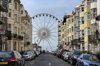 View through street with parked cars and apartment buildings on Ferris wheel