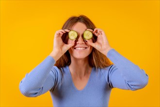 Vegan woman with cucumber slices on her eyes on a yellow background