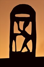 Wooden sculpture of African woman silhouetted against sunset