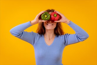Vegetarian woman in a portrait with peppers in her eyes on a yellow background