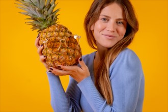 Woman smiling with a pineapple in sunglasses in a studio on a yellow background