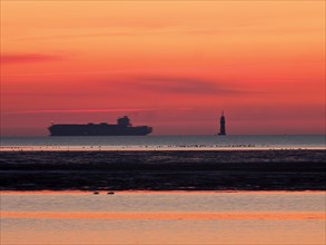 Container freighter on the Outer Weser with lighthouse in the evening light