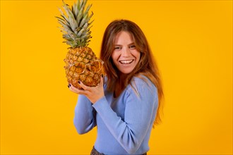 Girl with a pineapple in sunglasses in a studio on a yellow background