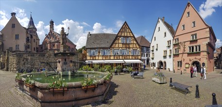 Panoramic photo of the Fontaine de Saint-Leon on the Pl. du Chateau Saint-Leon square with neo-Romanesque-Byzantine St. Leo Chapel and with medieval colourful buildings around the square in the centre...
