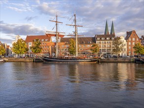 Historic sailing ship on the banks of the river Trave and behind it the brick buildings Old Hanseatic Houses in the Unesco World Heritage Site Luebeck