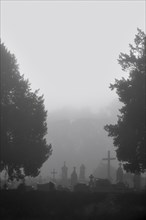 Silhouetted tombs and crosses at graveyard in the mist