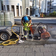 Road worker in protective clothing cutting asphalt at a road construction site