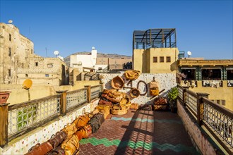 Variety of leather bags and pouffes exposed for sale on a terrace with a tannery view in Fes