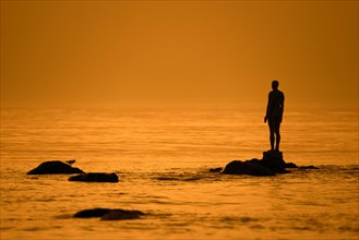 Sculpture Another Time XVI by Antony Gormley silhouetted against sunset along the North Sea coast at Knokke-Heist