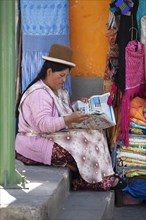 Bolivian woman wearing a traditional hat reading a newspaper