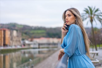 Blonde woman in blue dress with phone on the city river