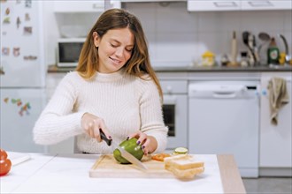 Vegetarian woman cooking a vegetable sandwich in the kitchen at home. cutting green pepper