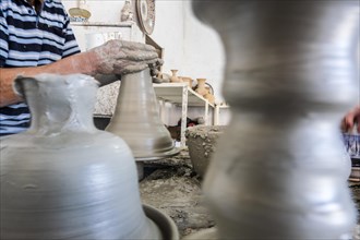 Skillful potter forming a vessel out of gray clay in a pottery factory