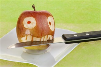 Apple with a face and a knife in its mouth