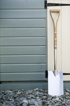 Stainless steel spade leaning against a wooden garden shed