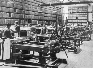 1890s black and white archival photo showing pressmen working on lithographic printing presses and racks for storing lithography stones in pressroom