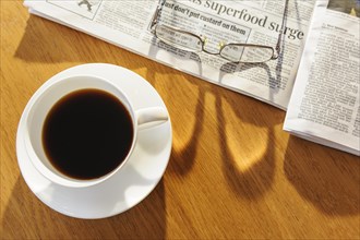 Overhead view of coffee cup newspaper and a pair of glasses