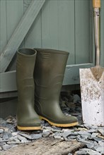 Pair of green wellington boots and a spade outside a garden shed
