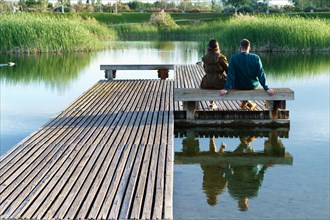 Young couple seen from the back sitting on the bank of a lake dock