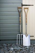 Garden fork and spade leaning against a painted shed