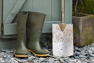 Pair of green wellington boots and a spade outside a garden shed