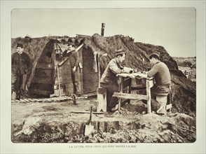 Soldiers sitting at a table outside shelter writing letters to home in Flanders during the First World War