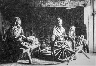Early 20th century photograph showing two old female home spinners using wooden spinning wheel and hackle