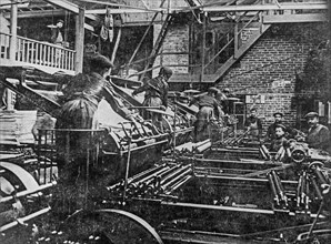 Early 1900s black and white archival photo showing pressmen and children working on lithographic printing presses in pressroom