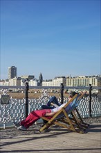 Tourists sitting on deckchairs on Brighton pier