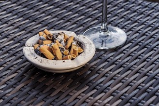 Ashtray full with cigarette ends on a rattan table