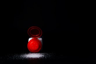 Close-up of a red salt shaker with spilled salt on a black table