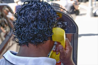 Black-haired New Yorker making a phone call at a telephone pillar with yellow handset
