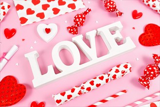 White Valentine's Day decoration LOVE text surrounded by seasonal decoration on pink background