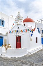 White Cycladic Greek Orthodox Church decorated with flags