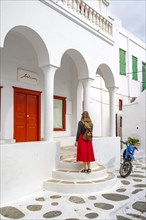Young woman in red skirt in front of a white Cycladic house with columns and red door