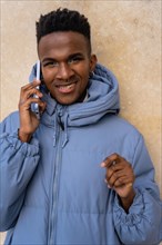 Portrait of a black ethnic man with a phone and a blue jacket on a yellow background