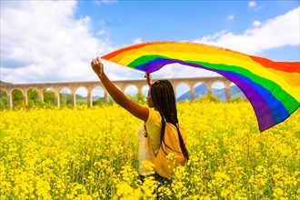 A black ethnic girl with braids holding the LGBT flag in a field of flowers