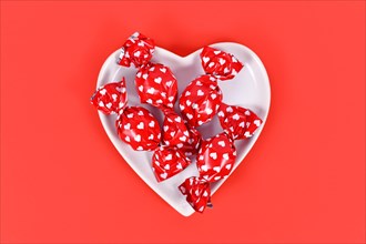 Candy wrapped in paper with hearts in bowl on red backgroun
