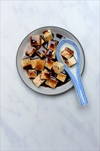 Soy sauce marinated tofu cubes in bowl with Asian ceramic spoon