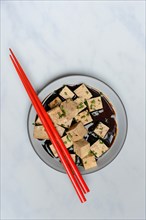 Soy sauce marinated tofu cubes in bowl with Asian chopstick